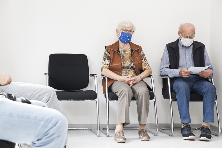Senior couple with face masks sitting in a waiting room of a hospital or an office